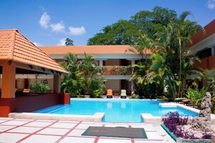 Un área de piscina con sillas de descanso, palmeras y un edificio con techo de tejas.