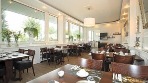 A restaurant with multiple dining tables, chairs, and large windows allowing natural light.