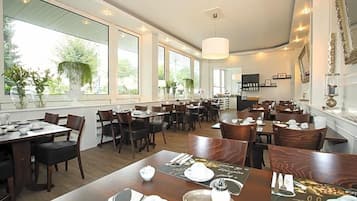 Un restaurante con varias mesas, sillas y amplios ventanales que dejan entrar luz natural.