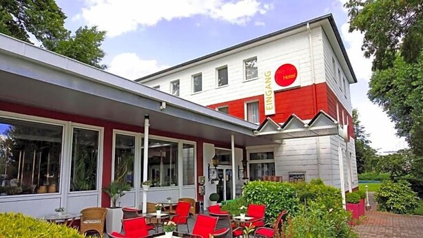 A hotel with a red and white facade, outdoor seating area with red chairs, and a garden.