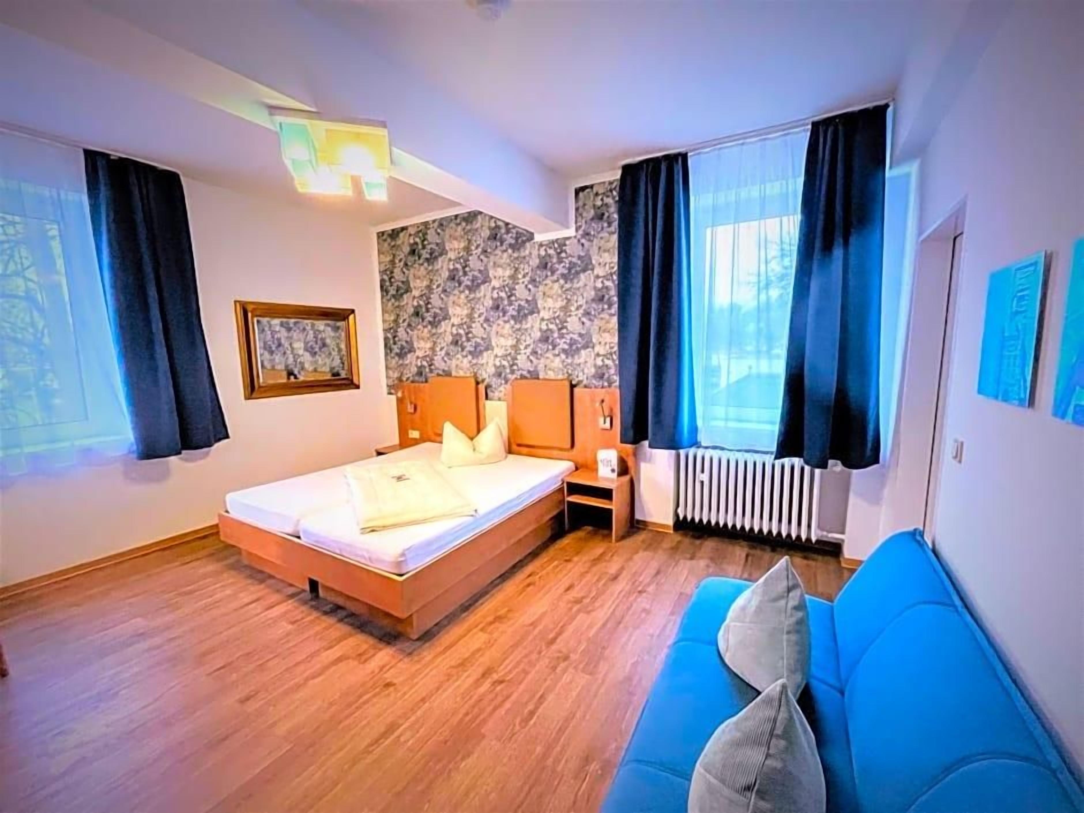 Ein Schlafzimmer mit einem Bett, einem blauen Sofa, einem Heizkörper und einem Fenster mit Vorhängen.