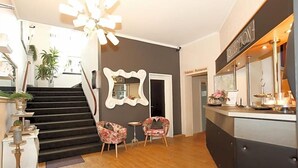 A reception area with a staircase, two floral armchairs, a mirror, and a reception desk.