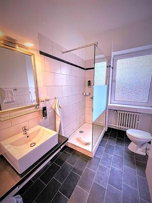 Un baño moderno con ducha acristalada, lavabo blanco y retrete.
