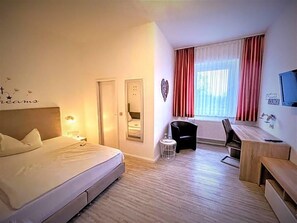 A hotel room with a bed, a desk, a chair, a small table, a mirror, and a window with curtains. - Arena Hotel (Gelsenkirchen)