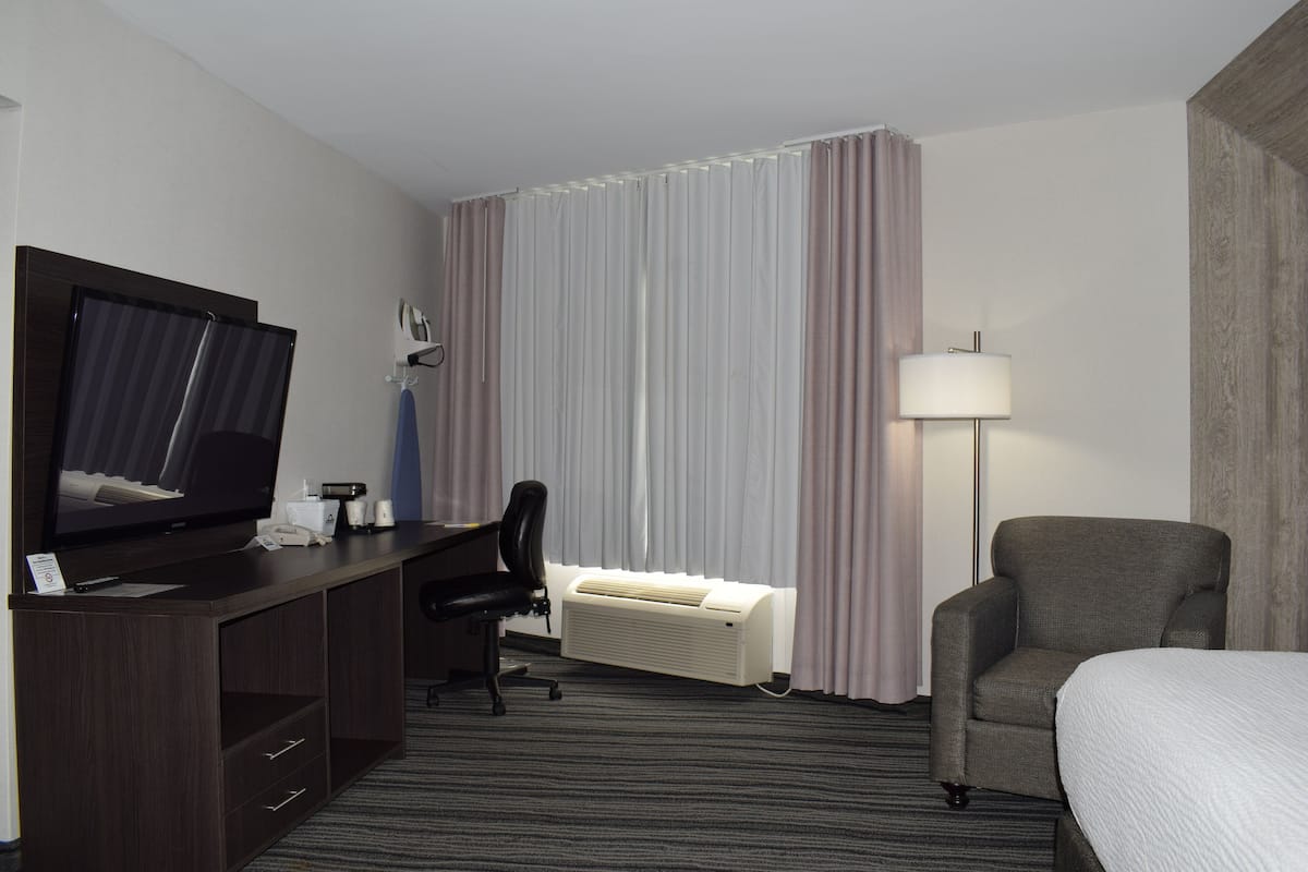 Habitación de hotel con cama, escritorio con televisor, una silla, lámpara y aire acondicionado.