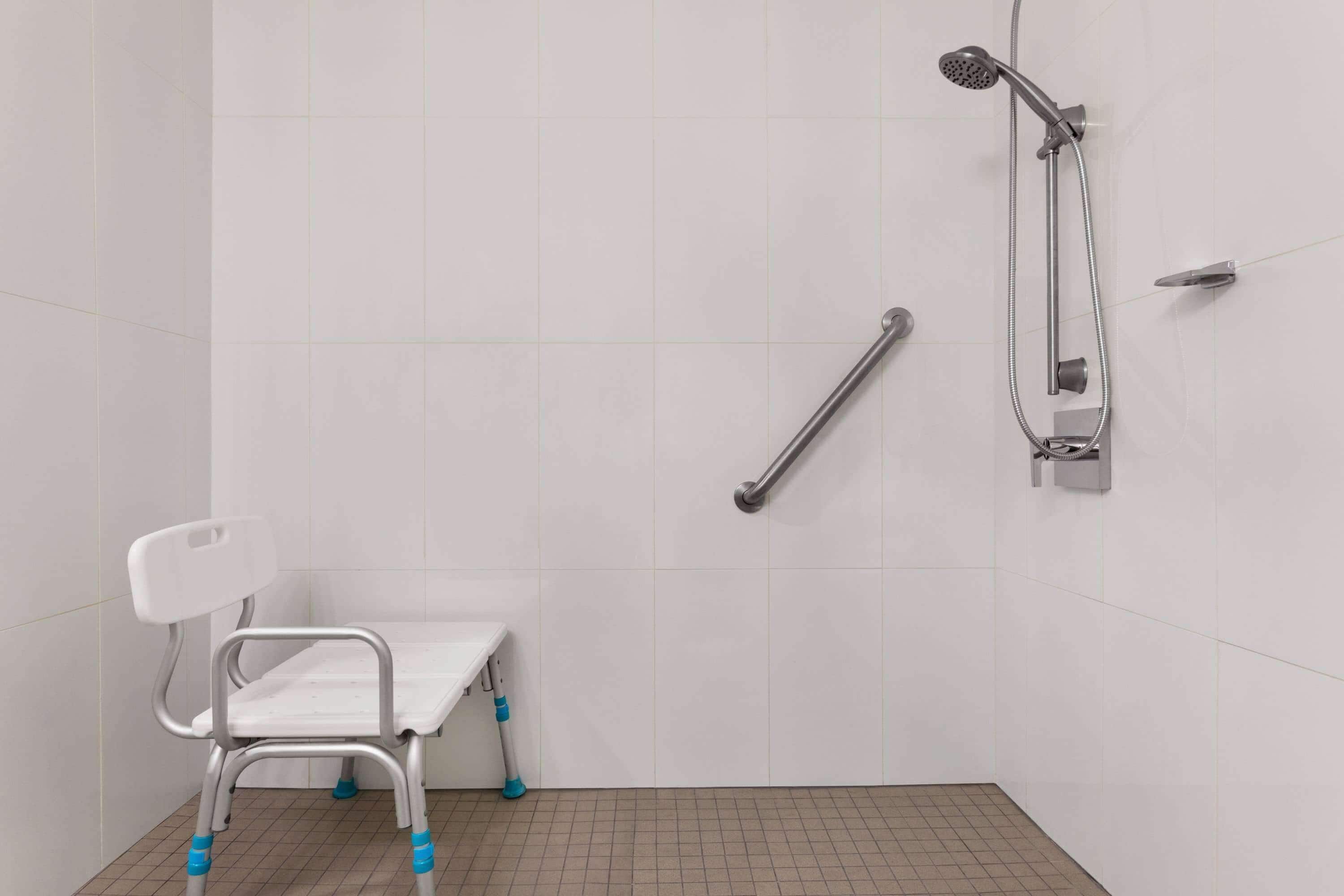 A bathroom with white tiled walls, a white sink, a shower with a handheld showerhead, and a grab bar.