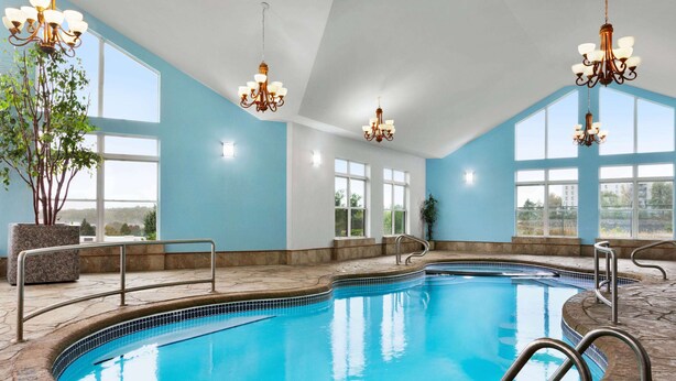 A large indoor swimming pool with clear blue water, surrounded by stone flooring, and equipped with metal handrails. - Days Inn by Wyndham Kingston (Kingston)