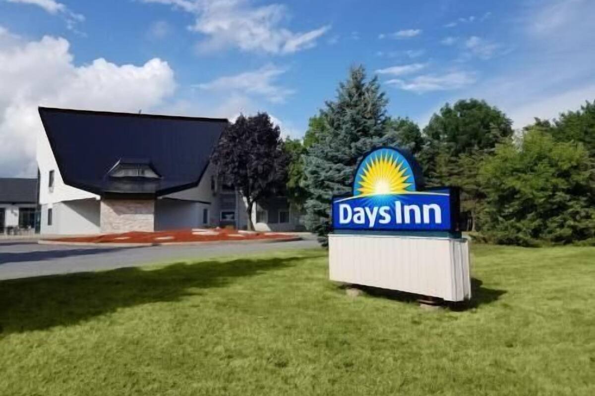 Letrero de Days Inn con logotipo de sol, un edificio de techo inclinado y un área verde al frente.