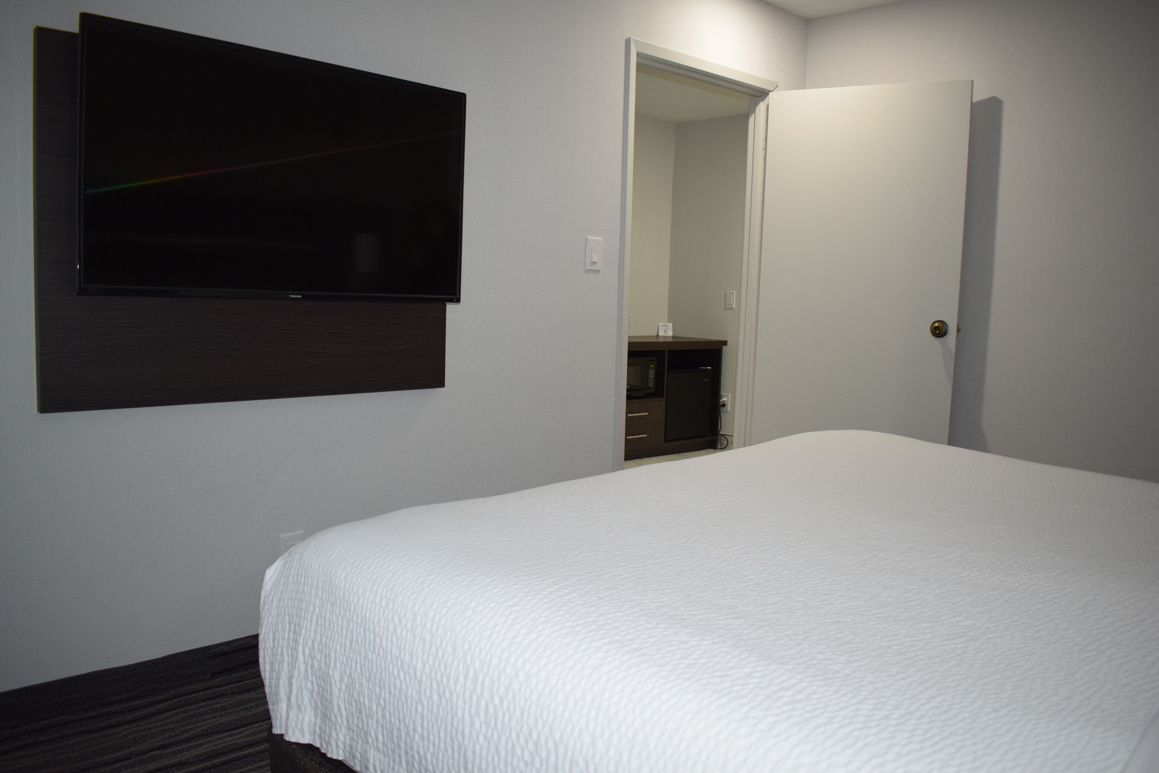 A hotel room with a large bed, a flat-screen TV mounted on the wall, and a door leading to a bathroom.