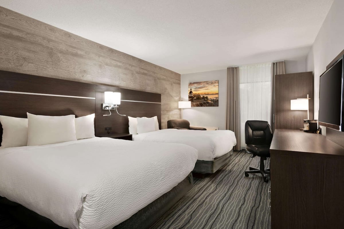 Una habitación de hotel con dos camas, un escritorio, una silla, un televisor y un cuadro en la pared.