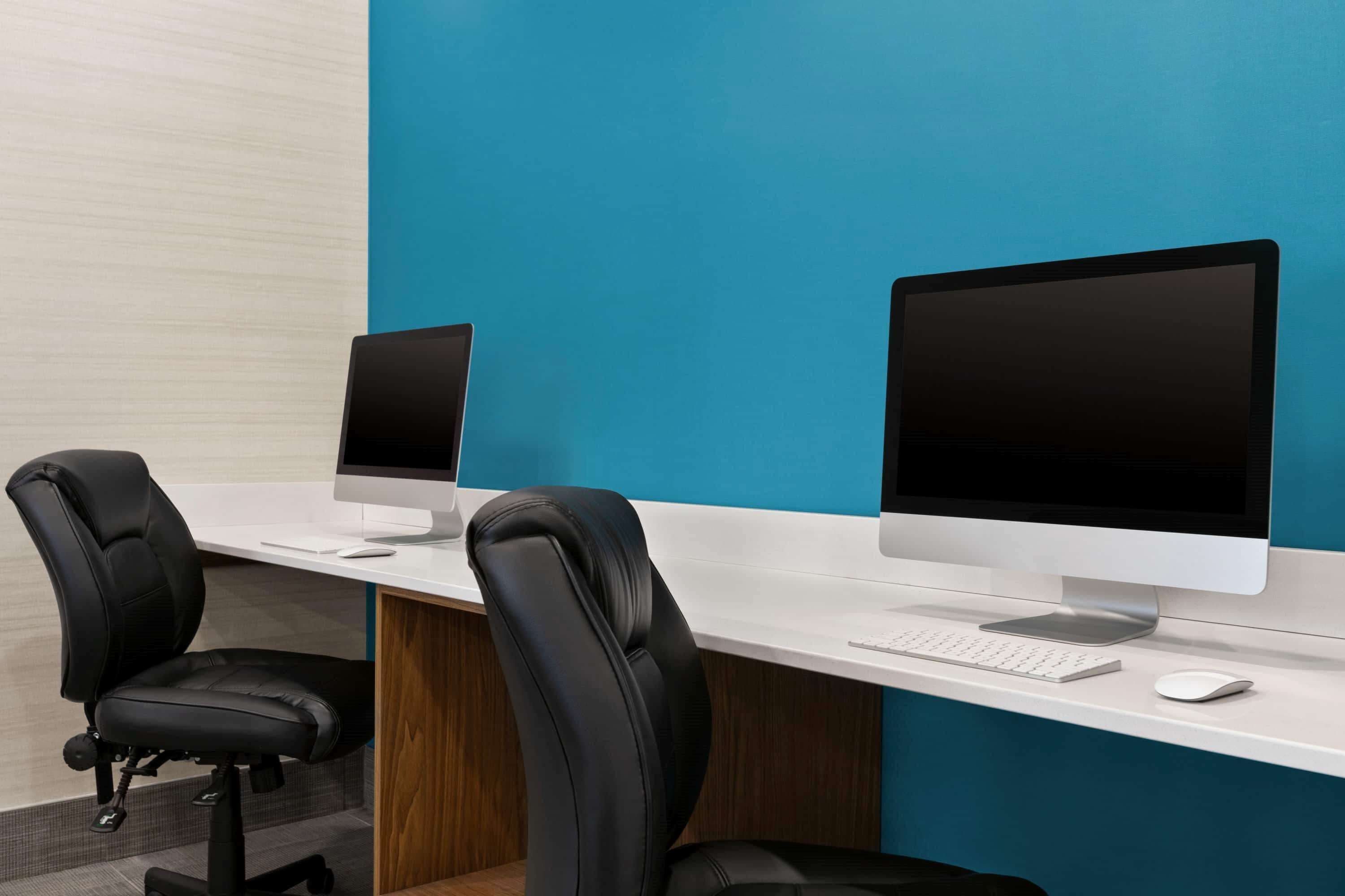 A modern office space with two desks, each with a computer monitor, keyboard, and mouse.