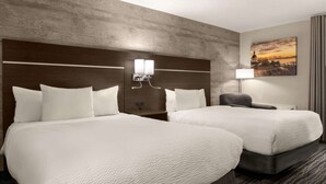 A hotel room with two beds, a headboard with wall-mounted lights, a nightstand, a lamp, and a cityscape painting on the wall. - Days Inn by Wyndham Kingston (Kingston)
