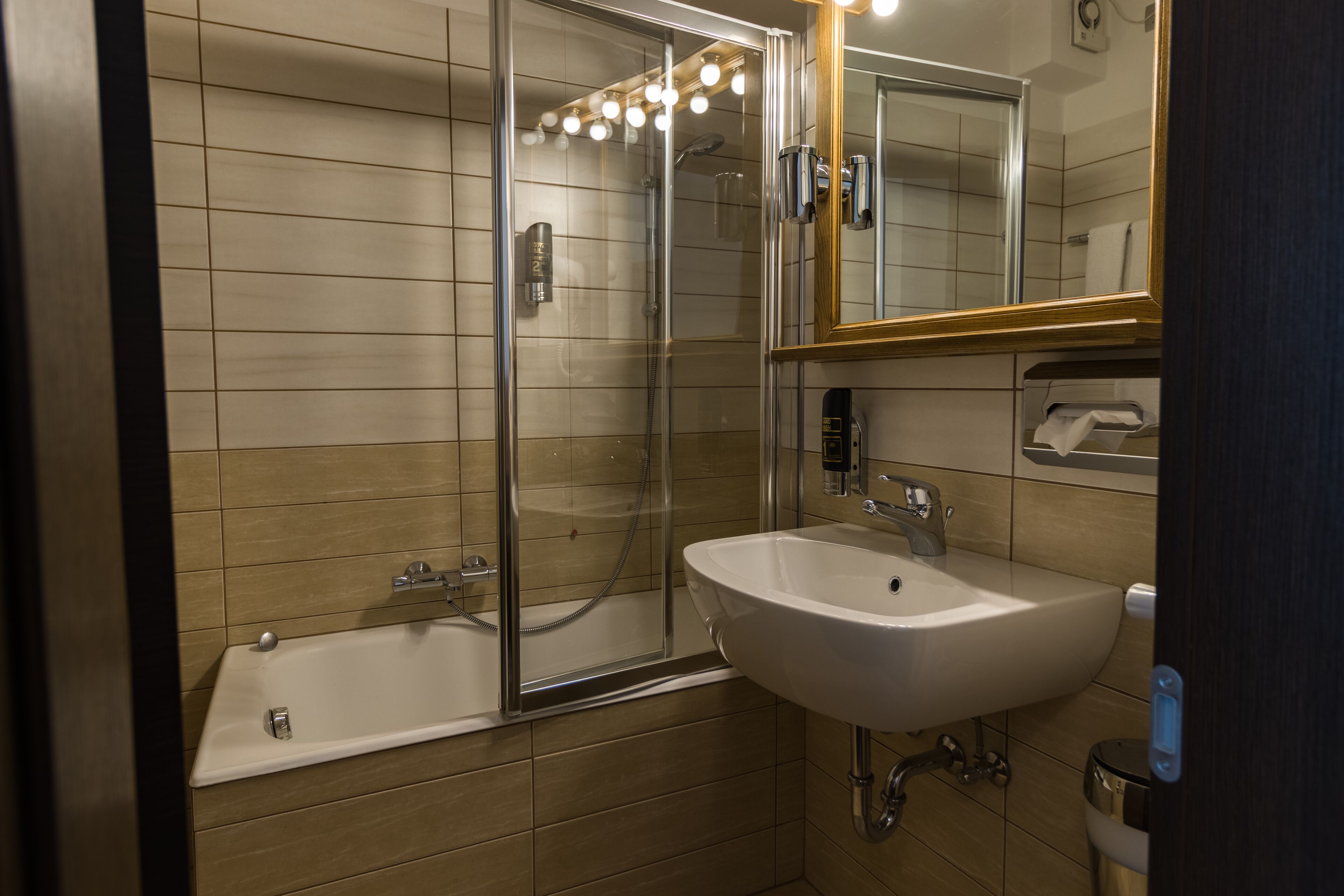 Ein modernes Badezimmer mit einer Duschkabine aus Glas, einem weißen Waschbecken und einem Spiegel mit Holzrahmen.