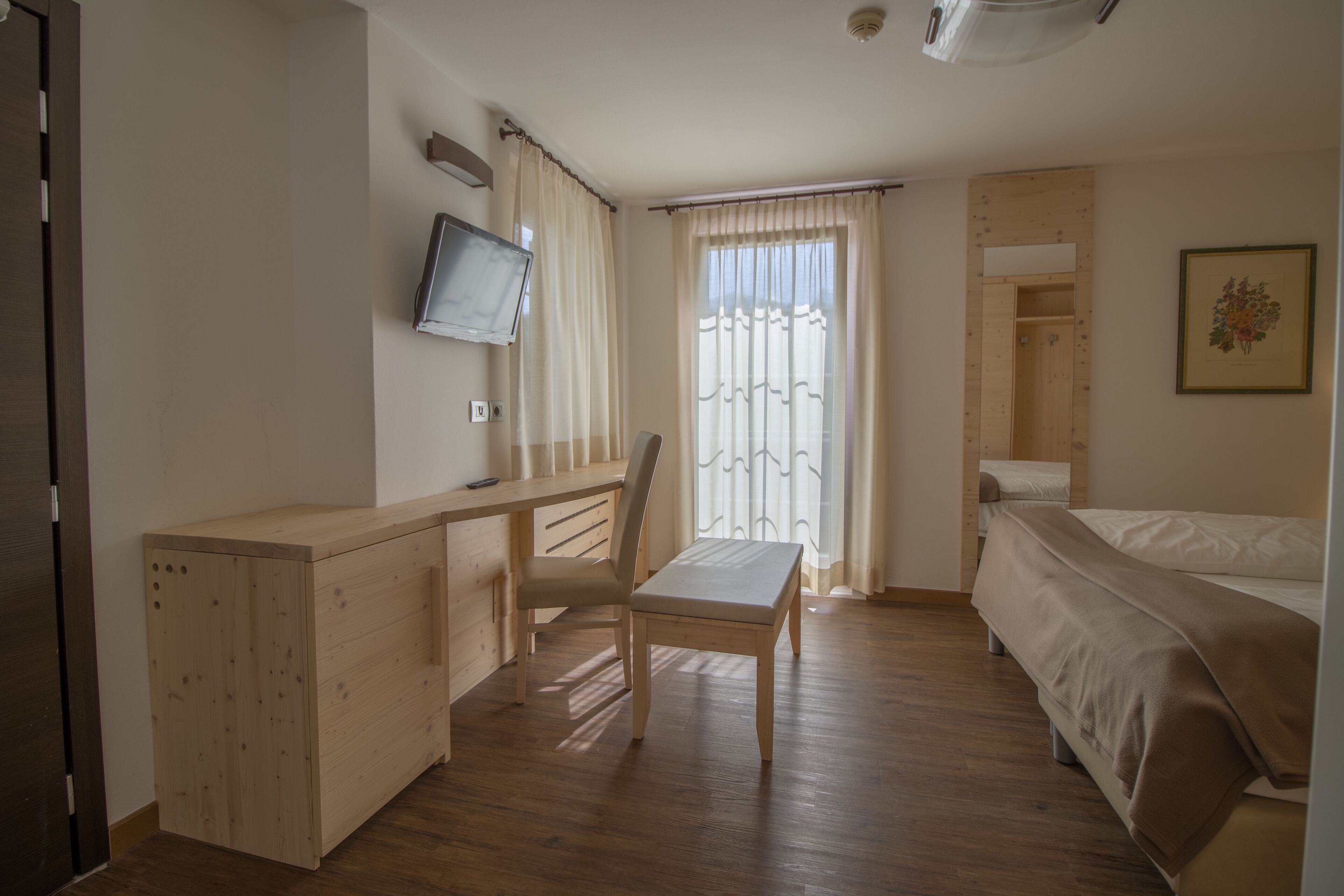 Un dormitorio con un escritorio de madera, una silla, una cama y un televisor montado en la pared.