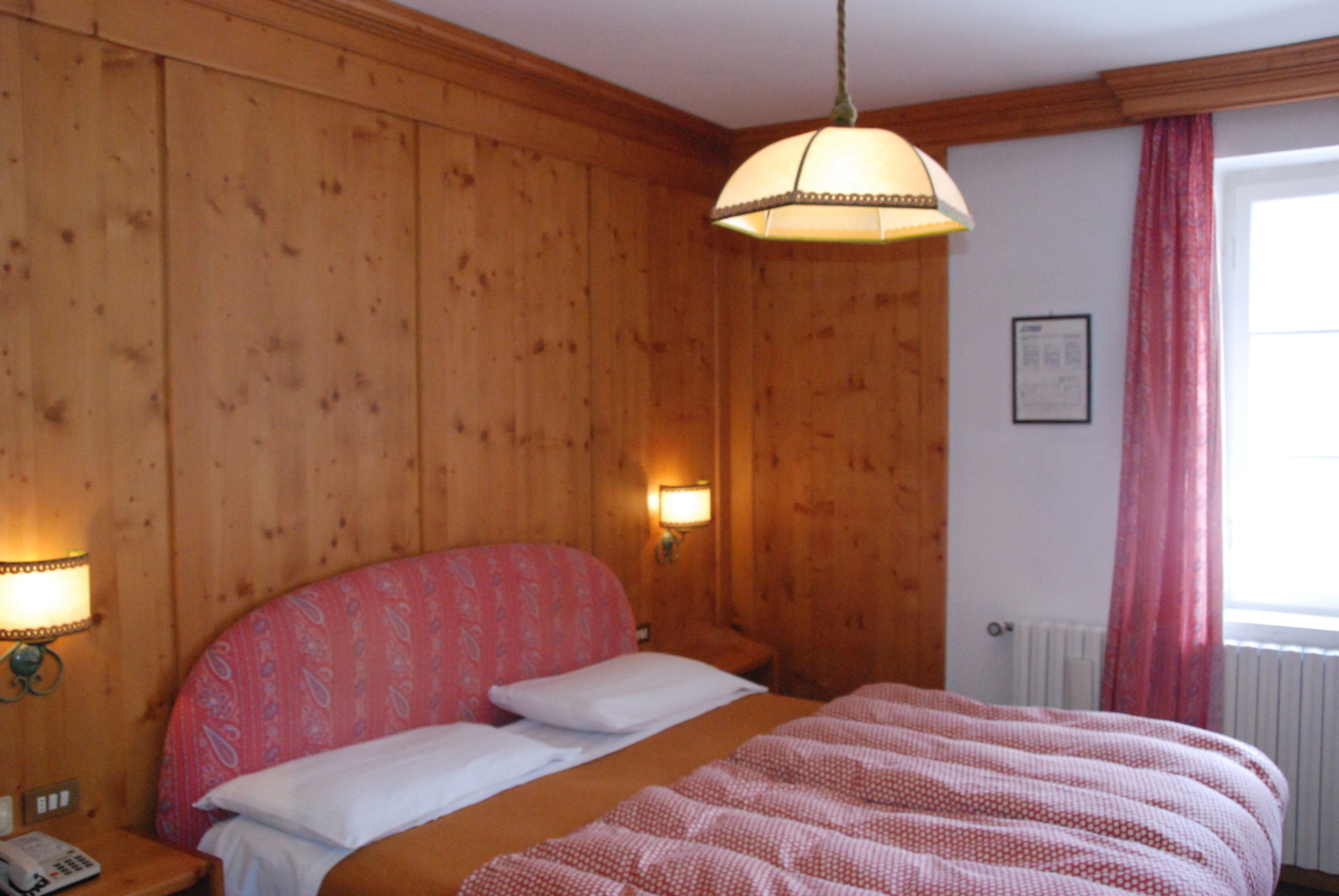 Une pièce aux murs lambrés, comprenant un lit, deux lampes fixées au mur et une fenêtre avec des rideaux.