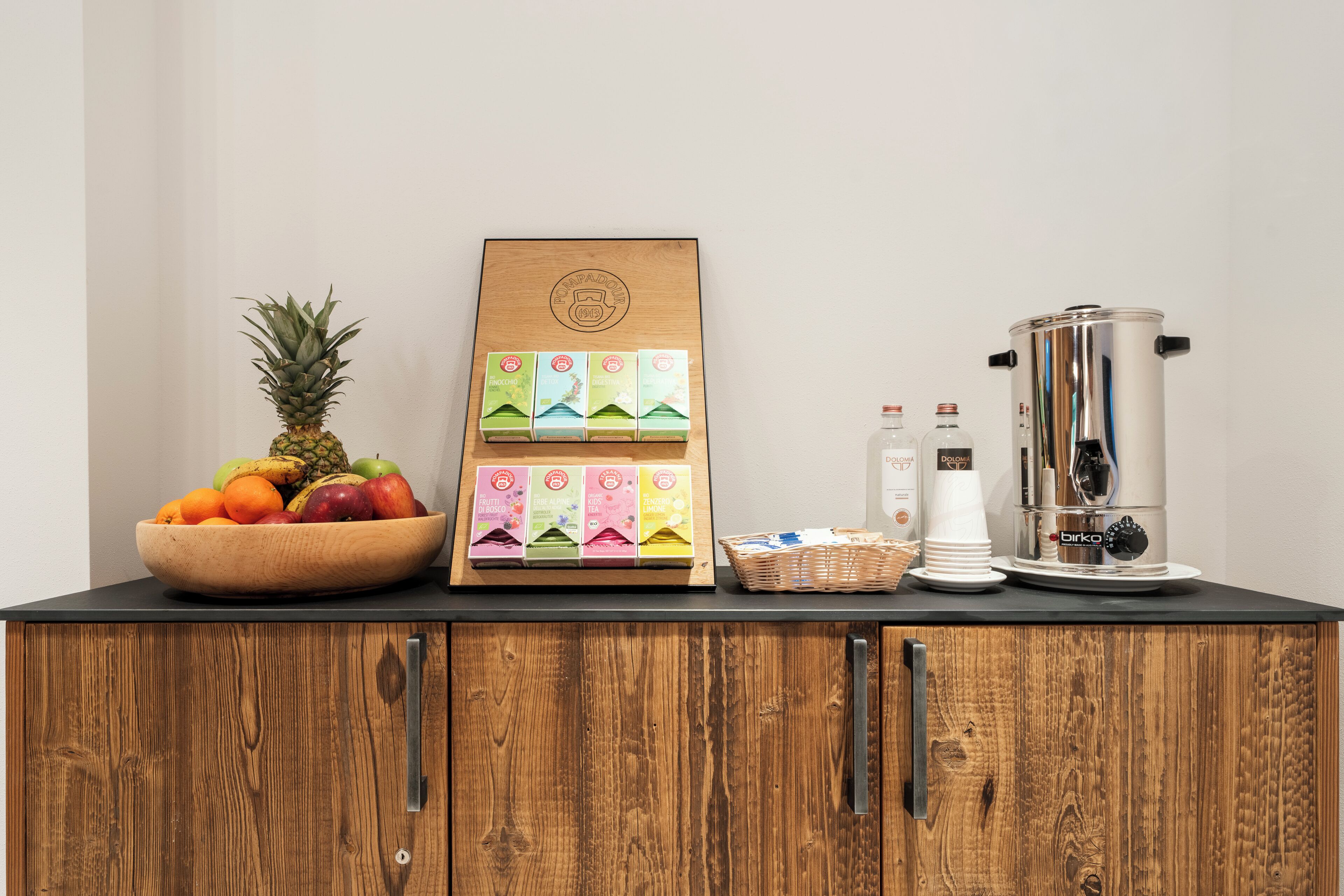 A wooden cabinet with a fruit bowl, a coffee grinder, and a coffee maker.