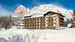 Ein mehrgeschossiges Hotel mit Balkonen vor einer verschneiten Berglandschaft.
