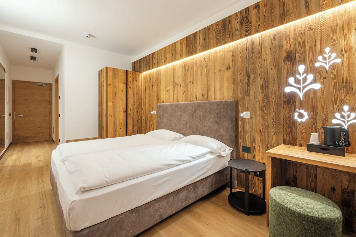Une chambre moderne avec un panneau mural en bois, un lit avec une literie blanche, une petite table de chevet et un pouf vert.