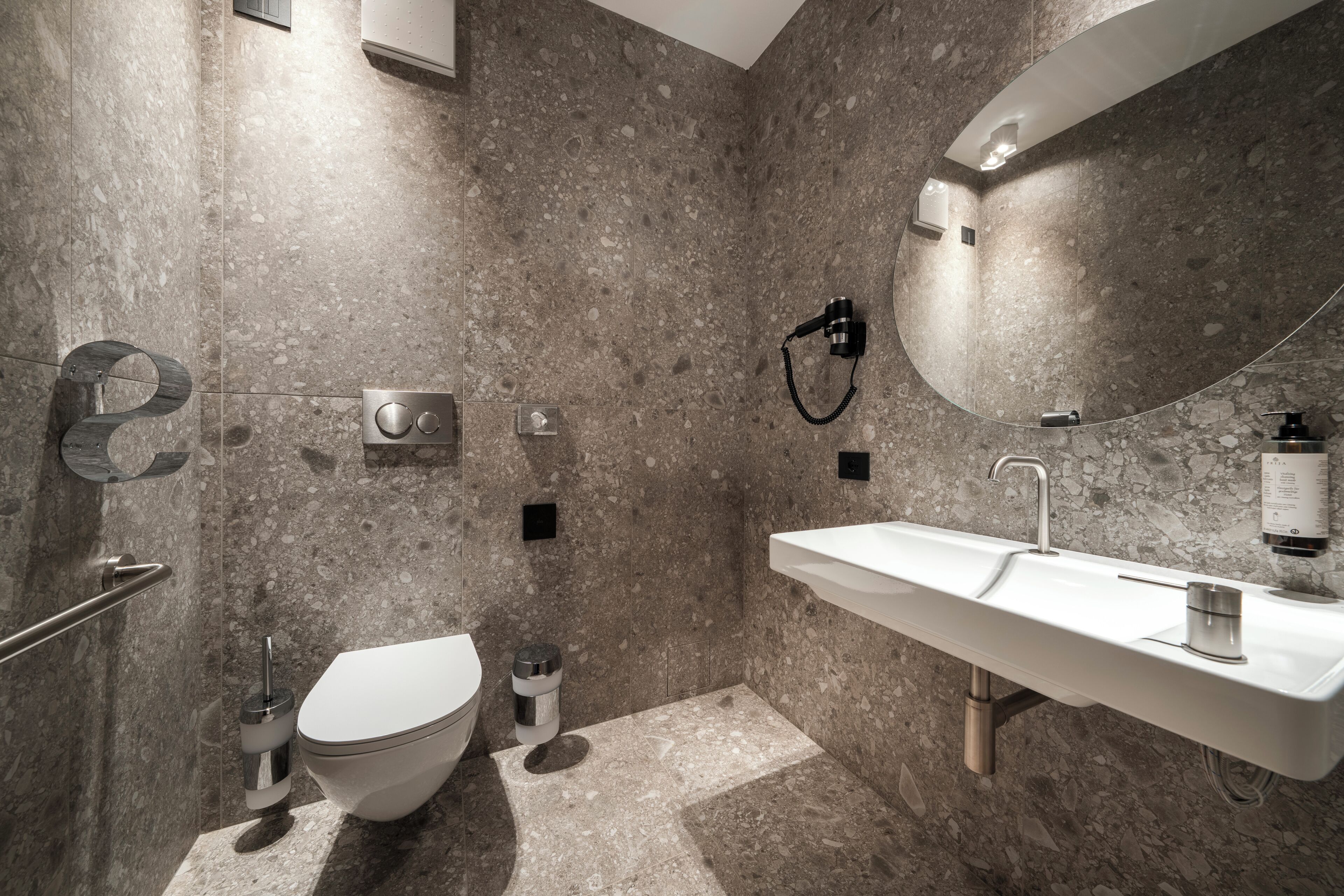 A modern bathroom with a marble floor, a white sink, a toilet, and a shower area.