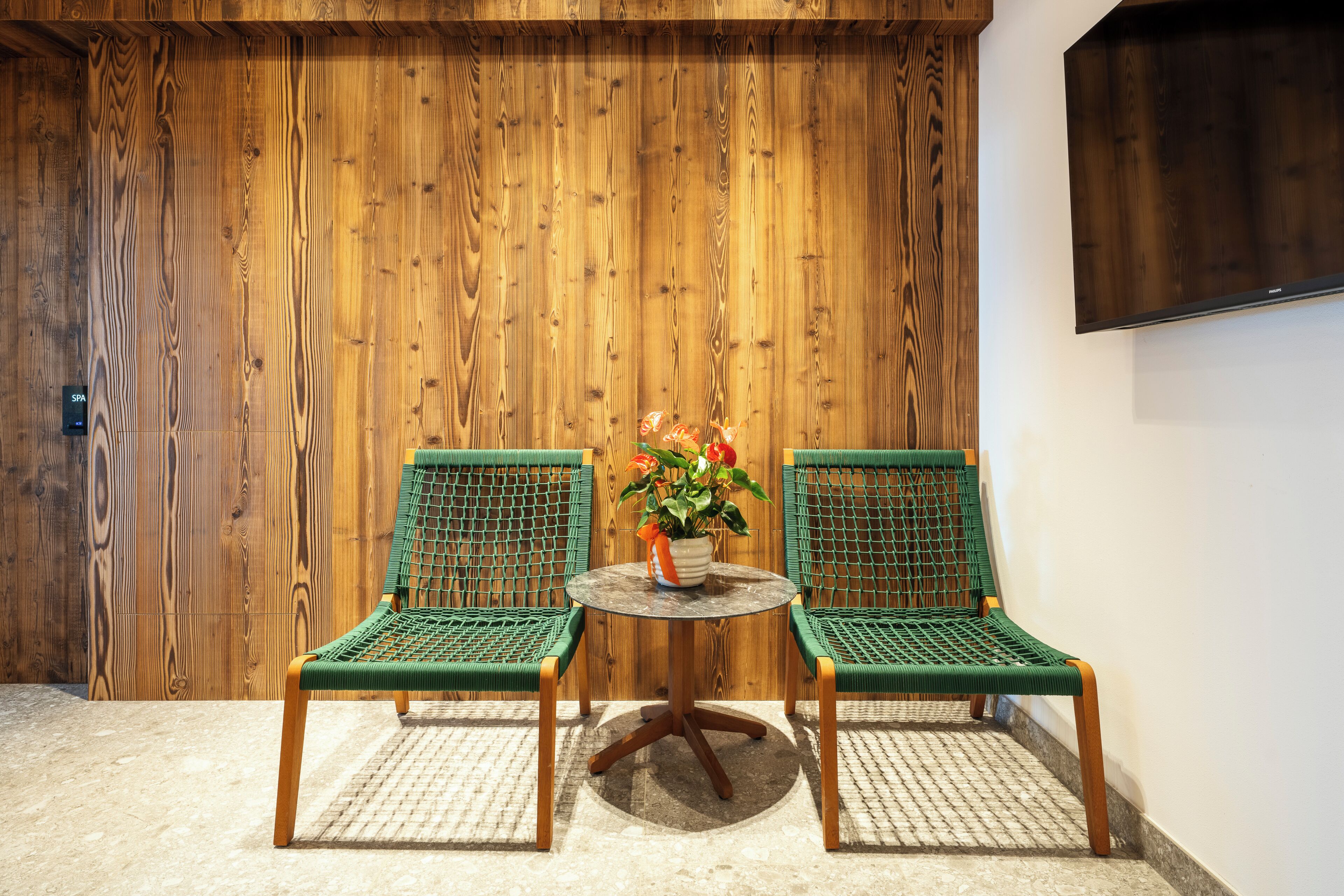 A room with a wooden wall, a round table with chairs, and a potted plant.