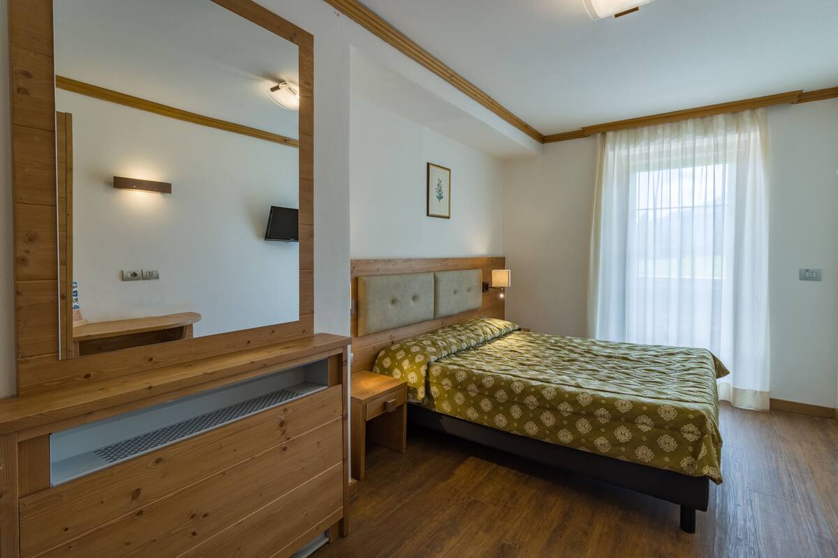 Une chambre à coucher avec une tête de lit en bois, un lit recouvert d’une couvre-lit à motifs, une table de chevet et un miroir.