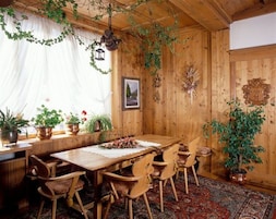 Ein Esszimmer mit Holzboden, einem Tisch und Stühlen, Topfpflanzen und einem hängenden Laternenleuchter.