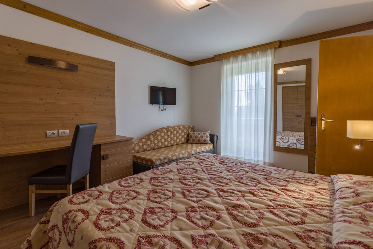 Une chambre à coucher avec un grand lit, un bureau, une chaise, une télévision et une fenêtre avec des rideaux.
