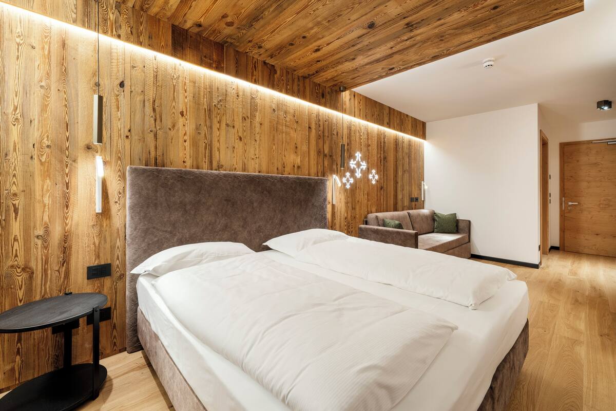 Une chambre moderne avec un panneau mural en bois, un lit avec une literie blanche, une petite table et un canapé.