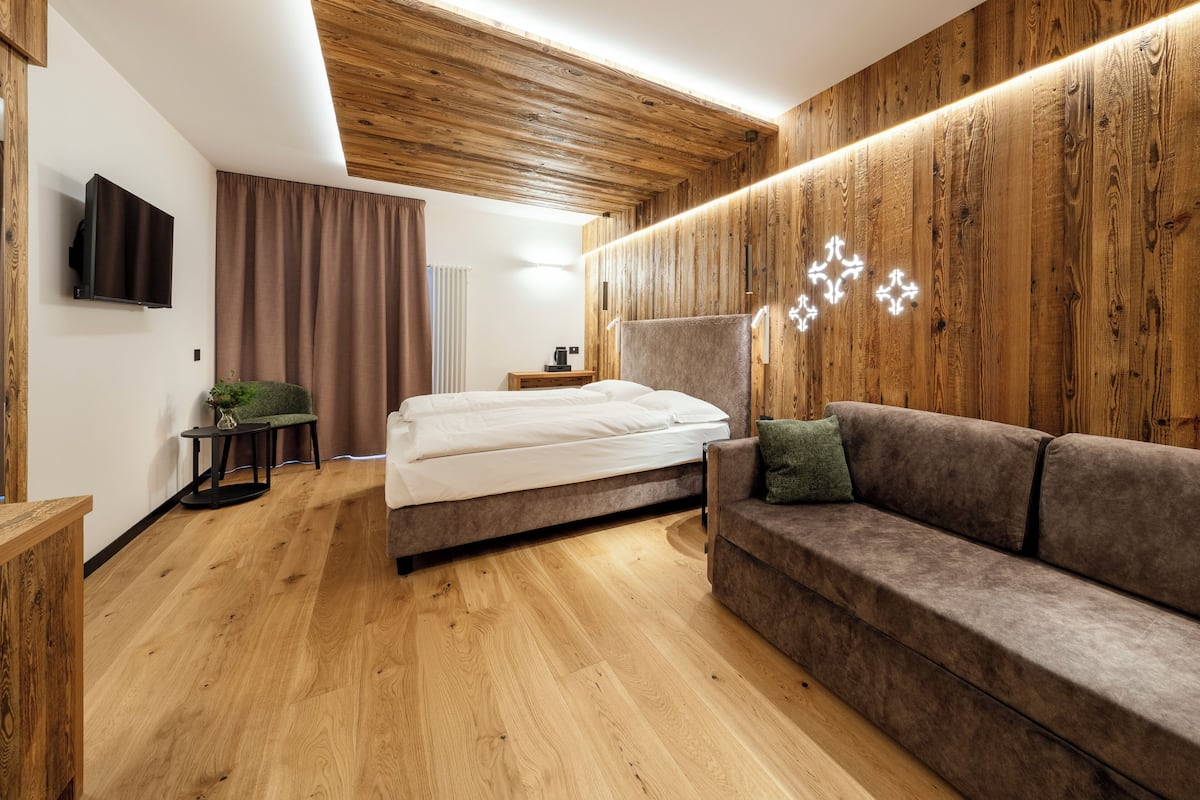 Une chambre d’hôtel moderne avec un plafond en bois, un lit, un canapé, une télévision et une petite table agrémentée d’une plante.