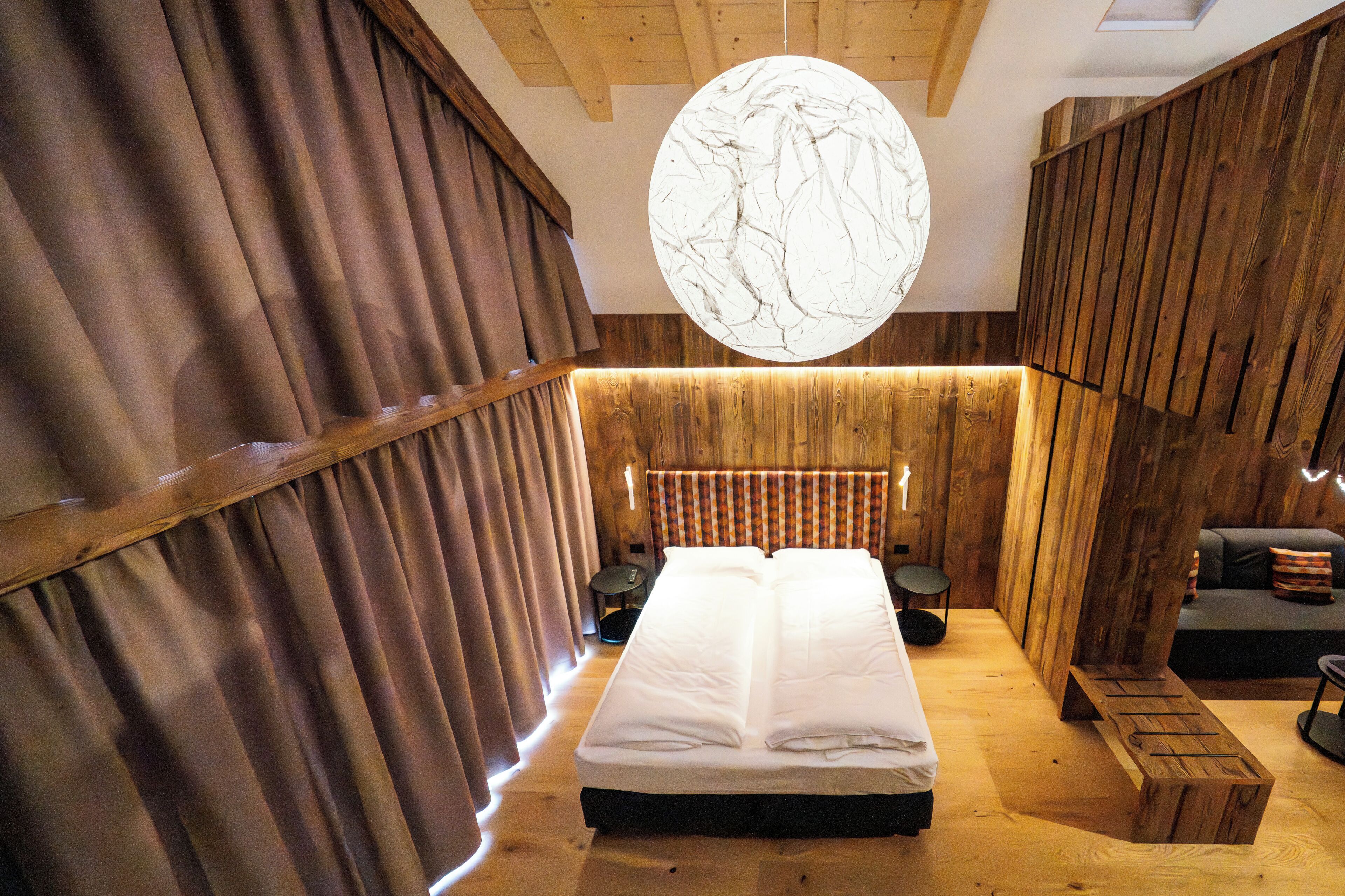 A wooden room with a bed, a round light fixture, and a bench.