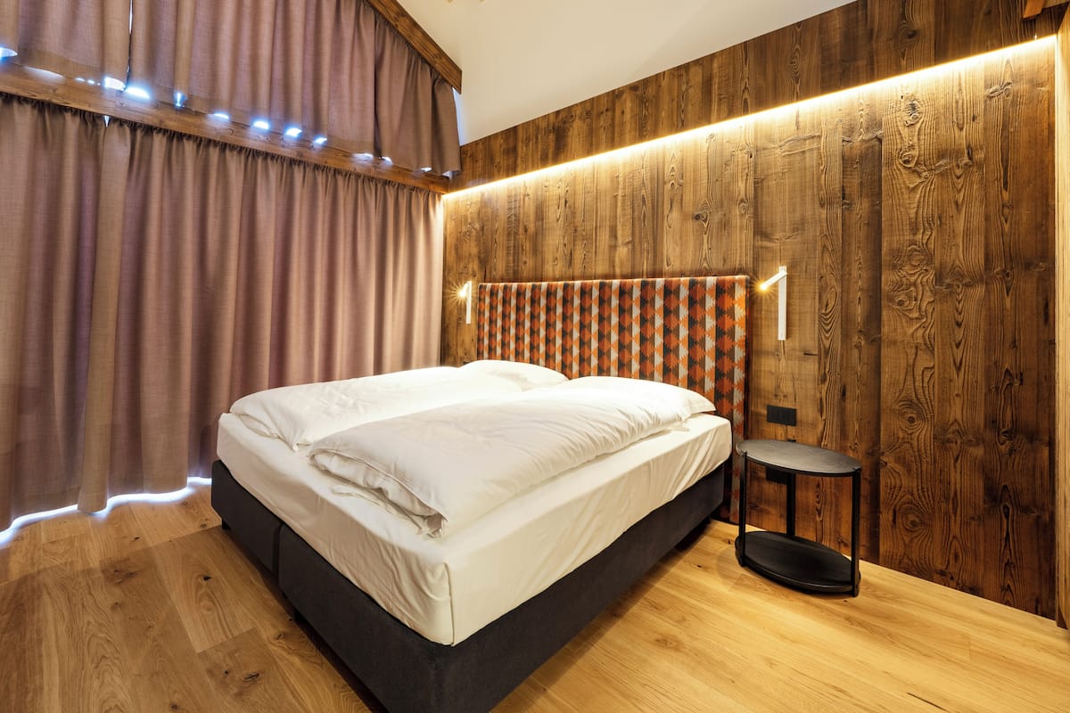 Une chambre à coucher moderne avec une tête de lit en bois, un lit recouvert de draps blancs, une petite table ronde et un rideau à motifs.
