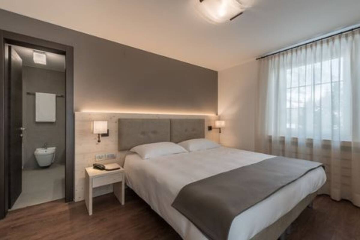 Une chambre d’hôtel moderne avec un grand lit, des lampes de chevet, une table de chevet, une salle de bain avec un lavabo et une serviette, et une fenêtre avec des rideaux.