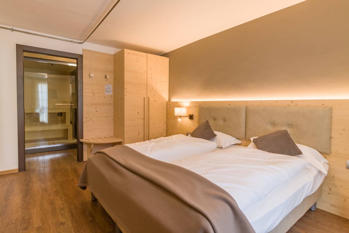 Une chambre d’hôtel avec une tête de lit en bois, un grand lit avec du linge de lit blanc, une table de chevet et une armoire.