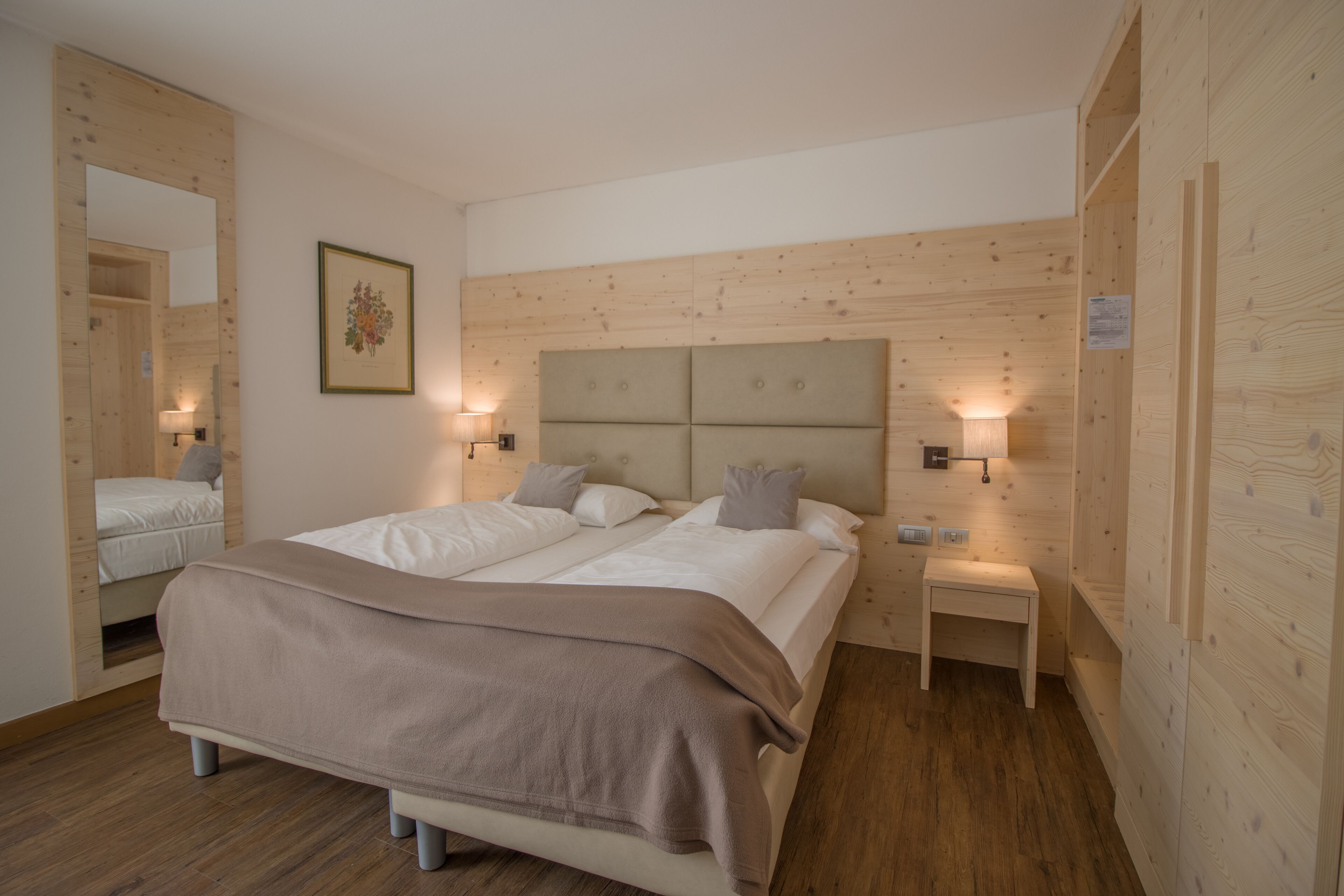 A double bed with a headboard, bedside lamps, a small table, and a mirror.