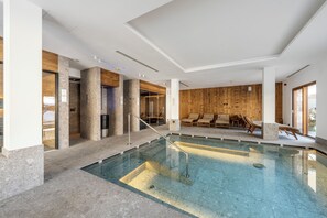 An indoor swimming pool with a clear view of the pool area, a wooden wall, and a seating area with lounge chairs.