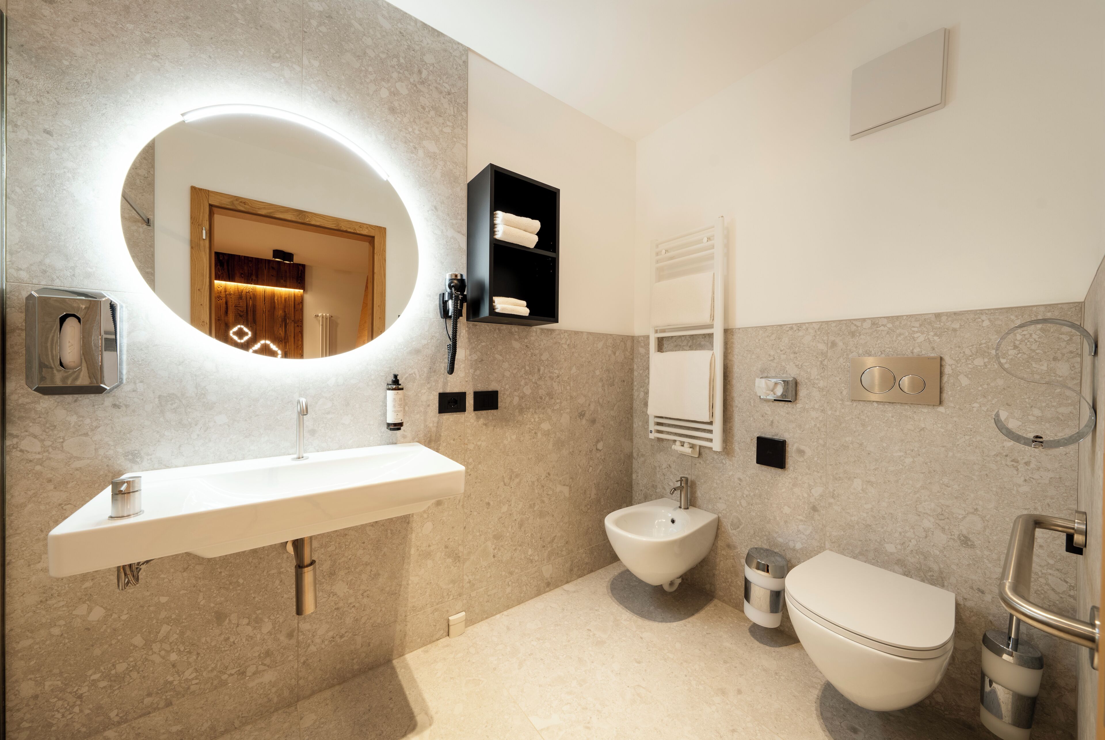 Un baño moderno con un espejo redondo, un lavamanos, un bidé y un inodoro.