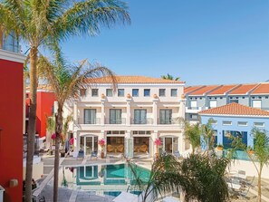 Un hotel de varios pisos con piscina, balcones y un edificio rojo contiguo.