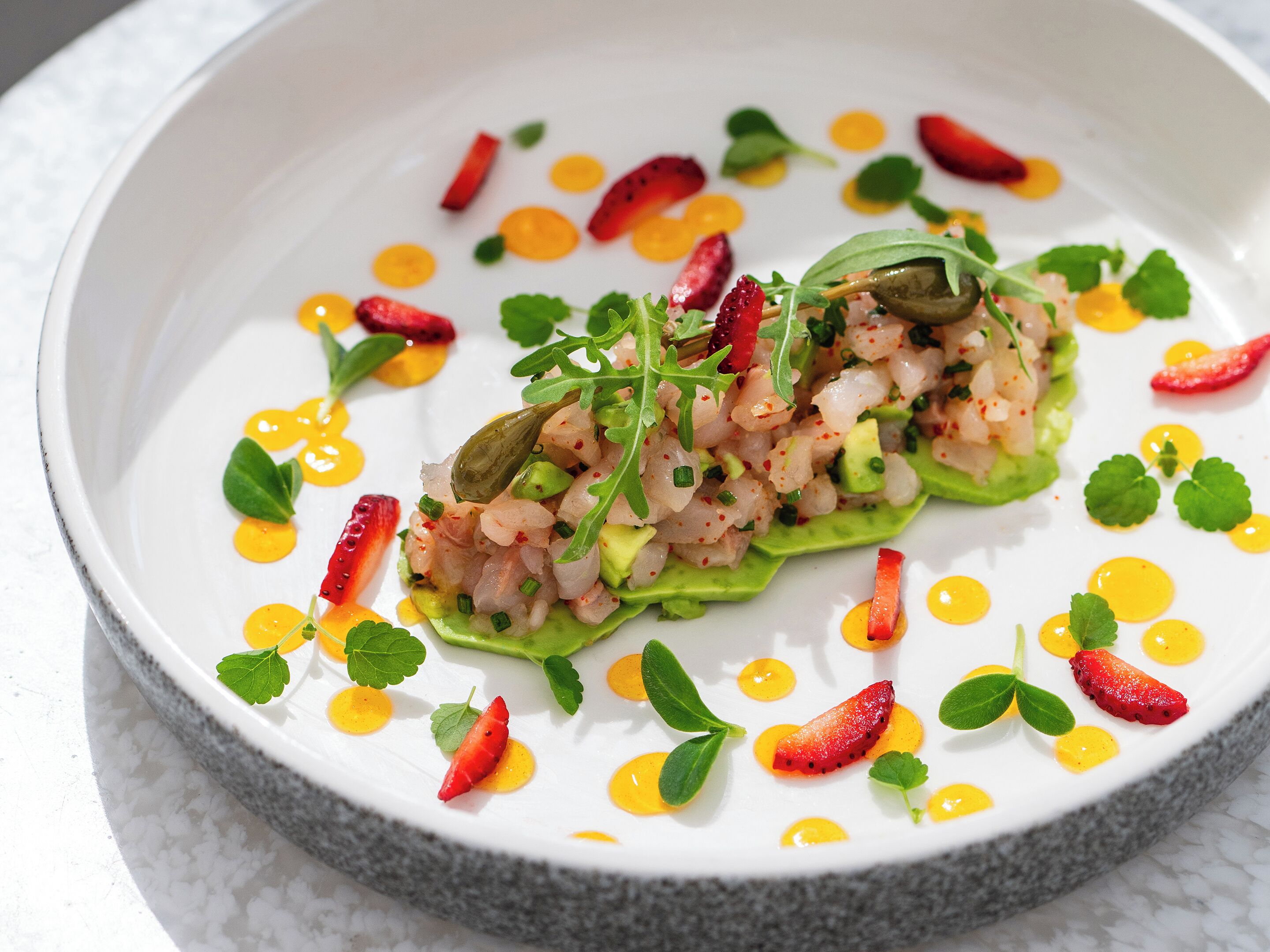 A white plate with a seafood dish, garnished with green leaves and red chili slices.