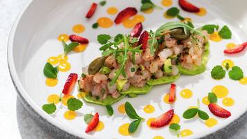 A white plate with a seafood dish, garnished with green leaves and red chili slices.