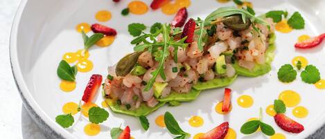 Un plato blanco con un guiso de mariscos, adornado con hojas verdes y rodajas de chile rojo.