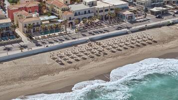 An aerial view of a coastal town with a beachfront promenade, beach umbrellas, and a variety of buildings including a market and residential structures.