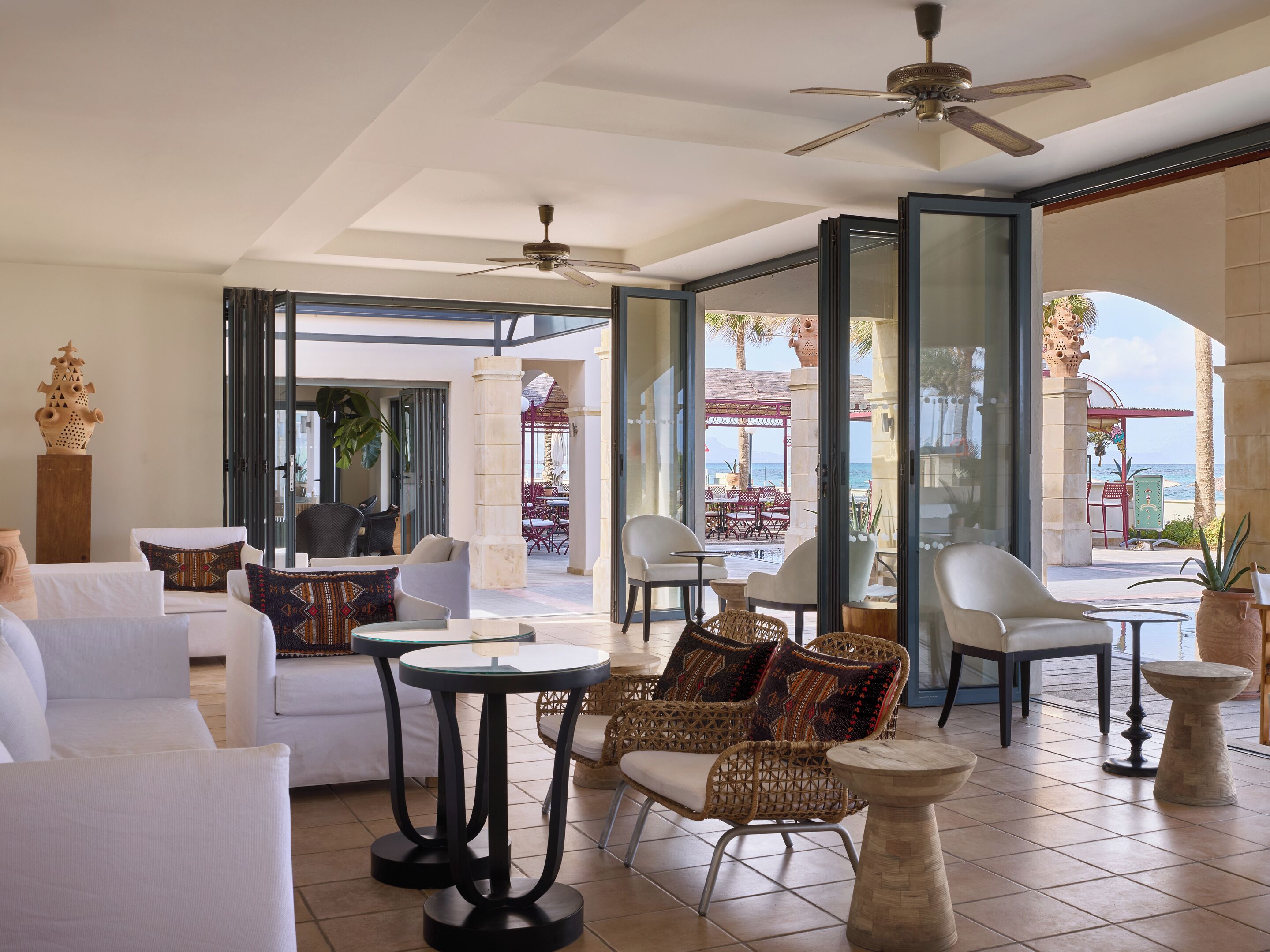 Un amplio salón con ventilador de techo, asientos cómodos y vista a la playa.