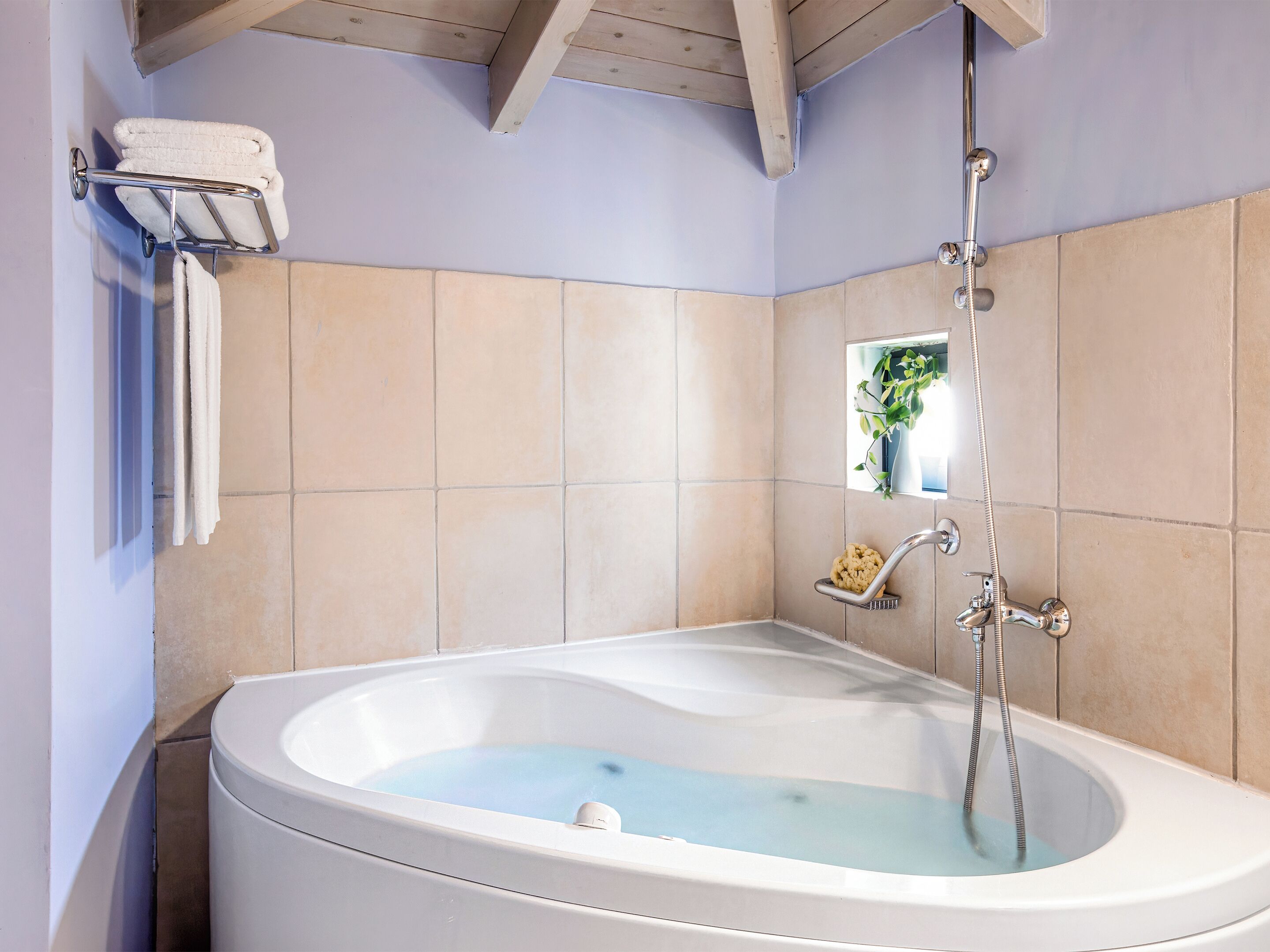 A bathroom with a bathtub, a towel rack, a showerhead, and a small window.