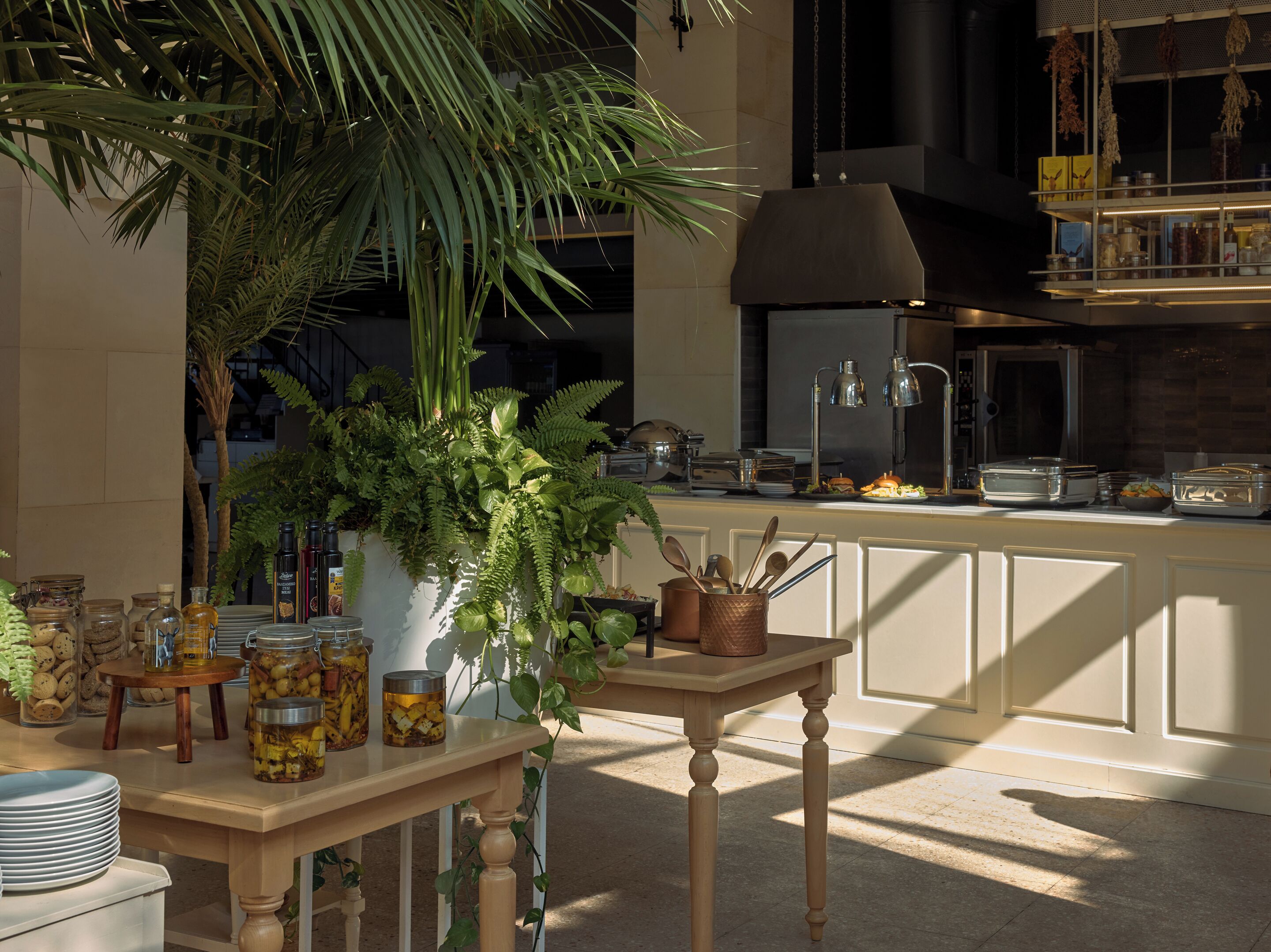 A well-lit kitchen with a large plant, a dining table with utensils, and a buffet area with food.