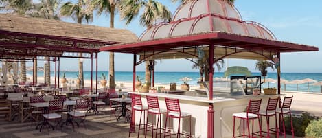 A beachside restaurant with outdoor seating, a pool, and a view of the ocean.