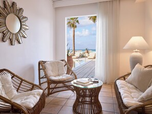 Una habitación con muebles de mimbre, una mesa redonda, un espejo grande y vista al mar.