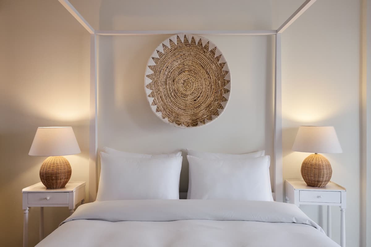 A neatly made bed with white linens, two bedside tables with lamps, and a woven wall hanging.