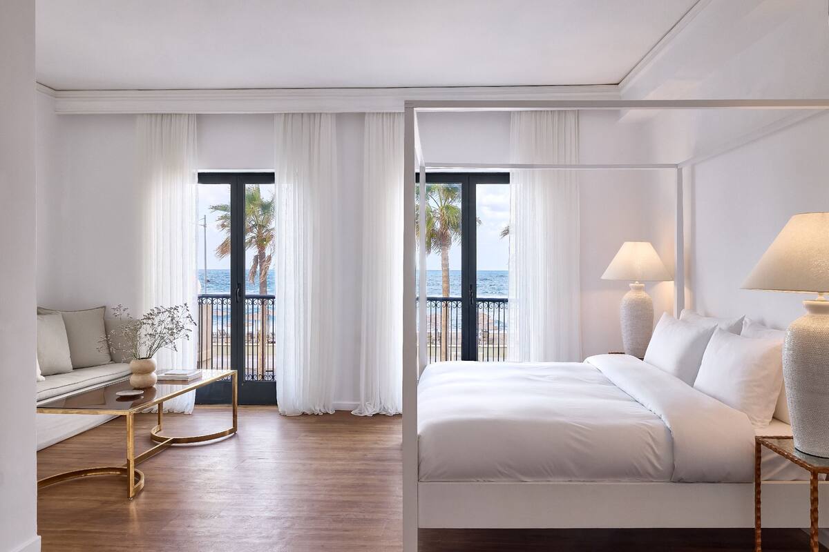 A hotel room with a balcony, a bed, a sofa, and a small table.