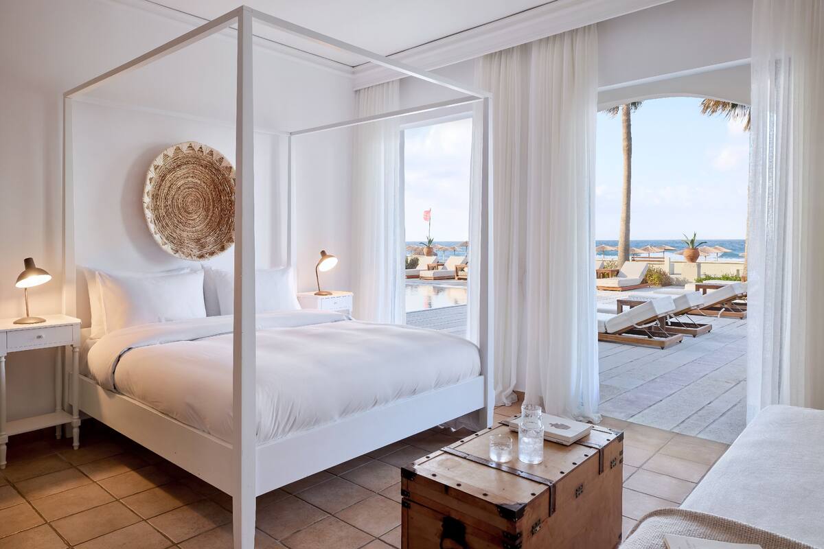 A four-poster bed with a view of a pool and beach.