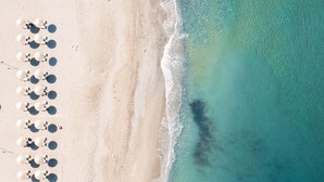 An aerial view of a beach with rows of umbrellas and lounge chairs, indicating a resort setting. - Grecotel Plaza Beach House (Rethymno)